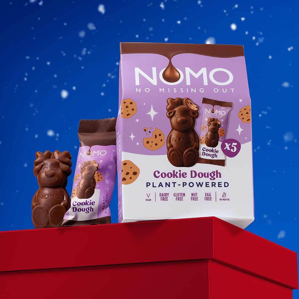 NOMO Cookie Dough plant-powered chocolate reindeer displayed on a red gift box against a blue snowy background. 